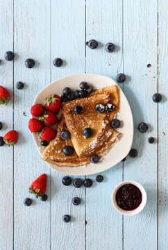 Delicious Crepes Breakfast with Dramatic light over a vintage wood background. An healthy meal of Pancakes with marmalede, blueberries and strawberries.