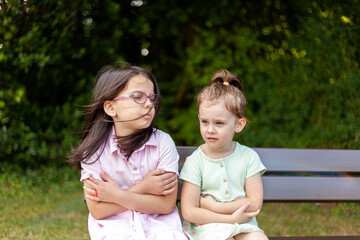 Two little girls sitting on a bench in the park and looking at each other