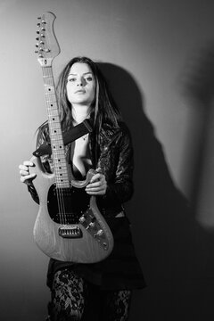 Photo of a sexy brunette woman standing and holding an electric guitar.