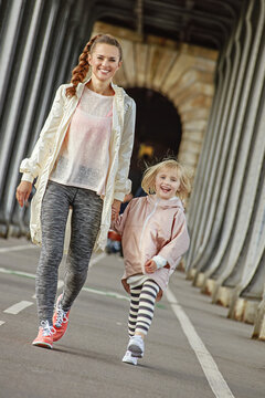 Year round fit & hip in Paris. Full length portrait of smiling healthy mother and daughter in sport style clothes on Pont de Bir-Hakeim bridge in Paris going forward