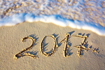 2017 inscription written in the wet beach sand with sea water wave.