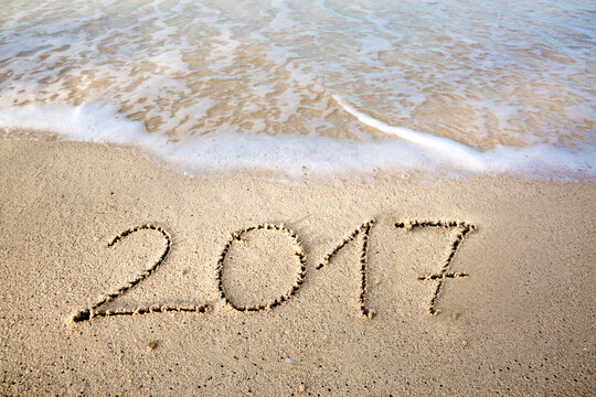 2017 inscription written in the wet beach sand with sea water wave.