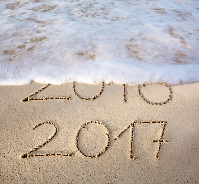 2016 2017 inscription written in the wet beach sand with sea water wave. Inscription 2016 and 2017 on a beach sand, the wave is almost covering the digits 2016.