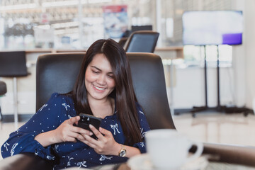 Smiling asian woman sitting on couch at office using smartphone. Beautiful asian use internet on phone for business.