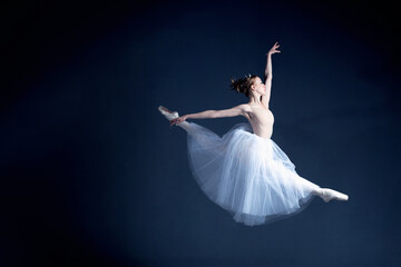 Young ballerina in a beautiful dress is dancing in a dark photostudio