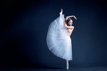 Young ballerina in a beautiful dress is dancing in a dark photostudio