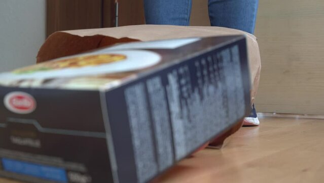 A bag of groceries tumbles at feet in sneakers, spilling boxes and food items onto the ground. A chaotic moment of unexpected mishap and mess.