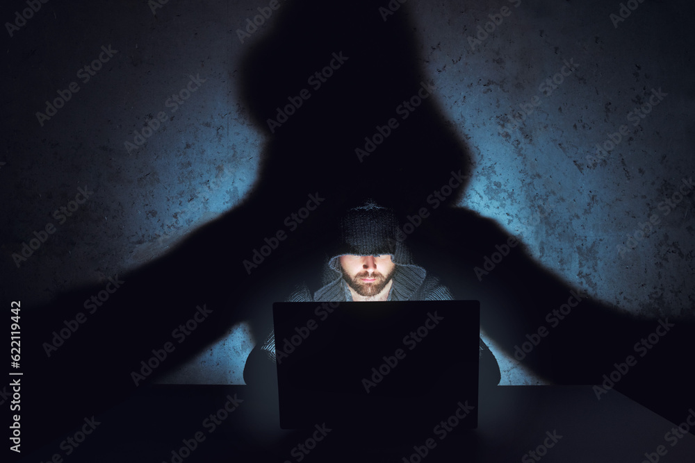 Aufkleber hacker works in dark empty room. his shadow is on the wall