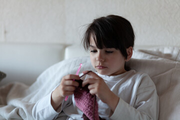 Little girl knits a sweater with a ball of yarn on the bed