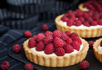 Delicious raspberry mini tarts (tartlets) with whipped cream on dark background