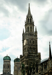 Fototapeta na wymiar Clock Tower MarienPlatz and Two Towers of Frauenkirche against Cloudy Sky Outdoors. Munich, Germany
