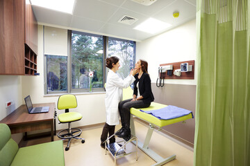 A general practitioner exams the lymph nodes of a beautiful young female patient in modern clinic.