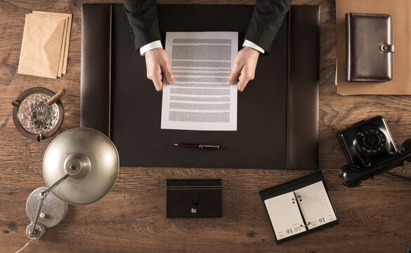 Vintage businessman in the office reading a contract sitting at his desk, top view