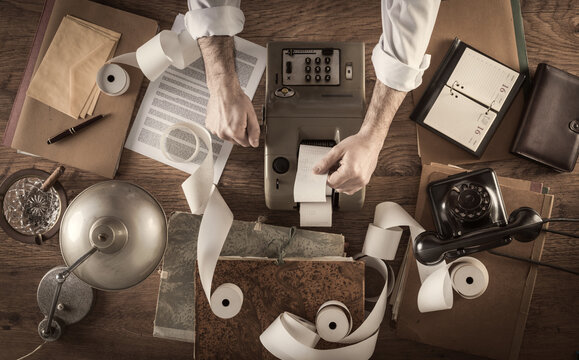 Messy vintage accountant's desktop with adding machine and paper rolls, he is working with the calculator
