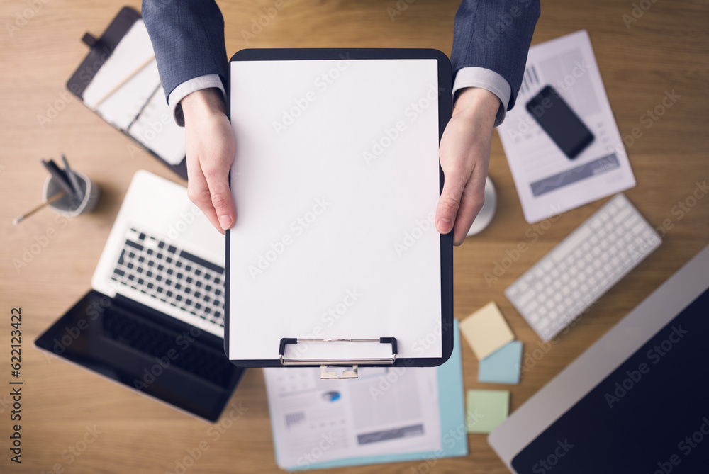 Aufkleber businessman working at office desk and showing a clipboard with a blank document, computers and stat