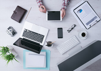 Businessman working at office desk and using a digital tablet, computer, laptop and various objects...