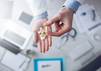 Doctor giving a lot of multicolor pills and tablets, hands close up with desktop on background, top...
