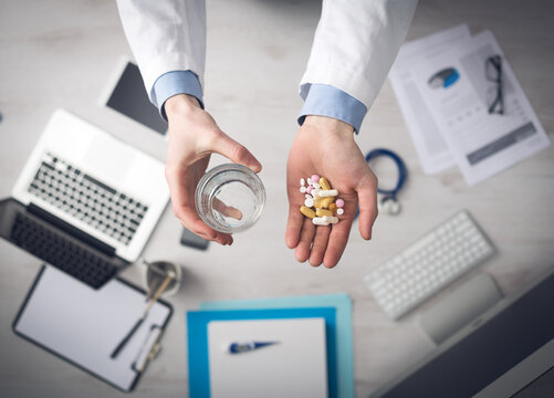 Doctor giving a lot of multicolor pills and tablets, hands close up with desktop on background, top view