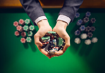 Elegant male casino player holding a handful of chips with green table on background, hands close...