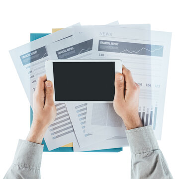 Businessman working at office desk with financial reports and using a touch screen tablet, hands close up, top view