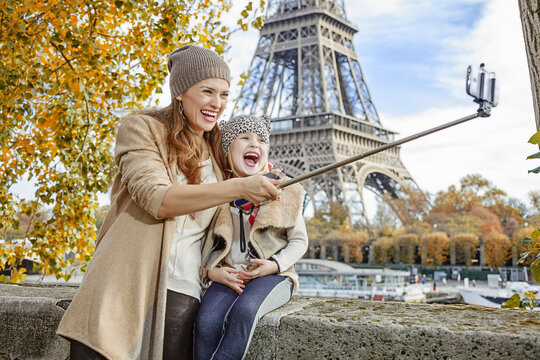 Autumn getaways in Paris with family. happy mother and daughter tourists on embankment near Eiffel tower in Paris, France taking selfie while sitting on the parapet