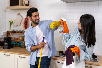 Young happy couple having fun while doing cleaning kitchen together