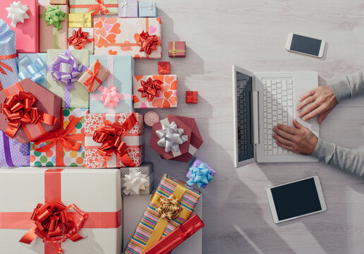 Man sitting at desk using a laptop with plenty of colorful gifts, celebrations and Christmas concept