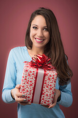 Joyful beautiful young woman holding a gift box with red ribbon