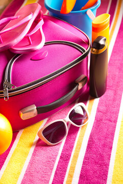 Striped colorful towel with pink bag, sunglasses and sun creams.