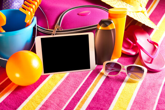 Empty touch screen tablet with colorful beach towel, sunglasses, sun creams and beach accessories.