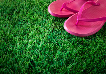Pink flip flops on green lush artificial grass, summer and vacations concept.