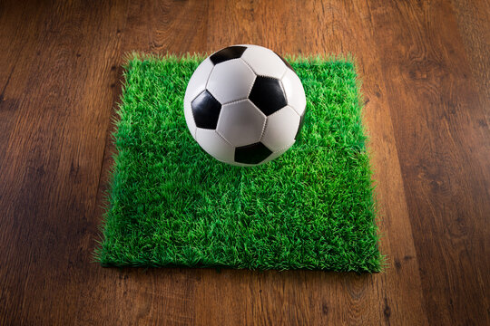 Soccer ball and artificial grass patch on hardwood floor.