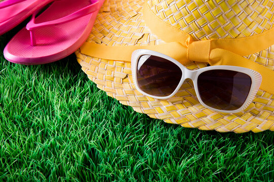 Sunglasses, straw hat and pink fli flops on lush green grass, vacations concept.