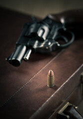 Obraz premium Vintage revolver gun on leather briefcase with bullet close-up.