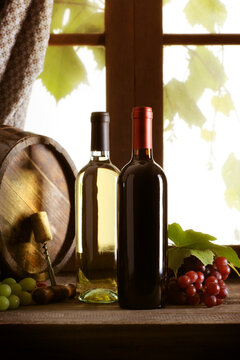 Wine bottles with grapes and barrel on old wooden table