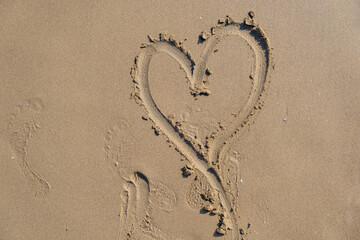 Drawing heart shape love concept on sand at the beach with vacation holiday summer travel background. Heart shape and footprint on wet sand.