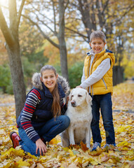 Fototapeta premium Cute kids and dog Labrador retriever posing in autumn park. Yellow and orange leaves around.