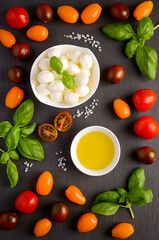 Italian food ingredients – mozzarella, tomatoes, basil and olive oil on black slate background, top view