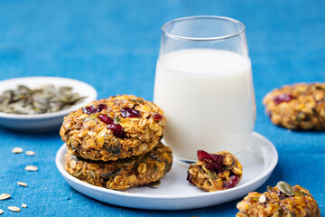Pumpkin, oat cookies with cranberries, maple glaze and glass of milk on a blue textile background