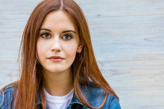 Outdoor portrait of beautiful thoughtful girl or young woman with red hair wearing a blue jeans denim jacket and white t-shirt