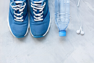 Flat lay sport shoes, bottle of water and earphones on gray concrete background. Concept healthy lifestyle, sport and diet. Focus is only on the sneakers.