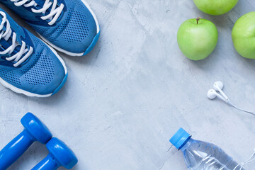 Flat lay sport shoes, dumbbells, earphones, apples, bottle of water on gray concrete background....