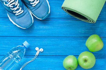 Flat lay sport shoes, bottle of water, mat and earphones on blue wooden background. Concept healthy...