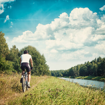 Rear View of a Cyclist Riding a Bike on River Bank. Healthy Lifestyle and Leisure Activity Concept. Toned and Filtered Instagram Styled Photo with Copy Space.