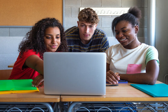 Multiracial group of high school students doing homework research together using laptop in class.