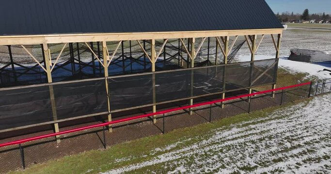Aerial video of an outdoor batting cage with a covered wooden structure.