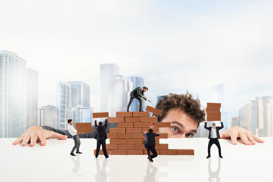 Businessman watches a teamwork of businesspeople work together by building a brick wall