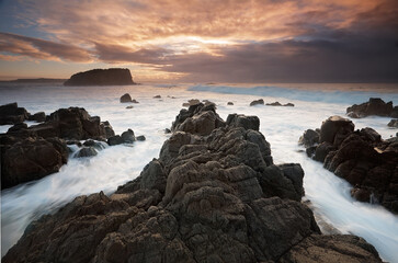 Ocean flows around the Minnamurra volcanic rock outcrop and views across to Stack Island formerly an extension of the rocks and cliffs here..  Taken at low tide during sunrise