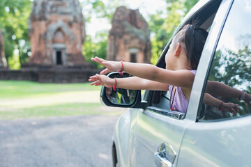 Happy girl in her car reaching outside the car, feeling the fresh air and warm sunshine during a trip.