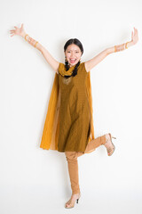 Portrait of excited mixed race Indian Chinese girl in traditional punjabi dress arms raised, full length standing on plain white background.